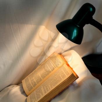 book on pillow lit reading lamp at night