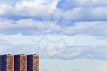 three brick modern houses under blue spring sky with afternoon clouds