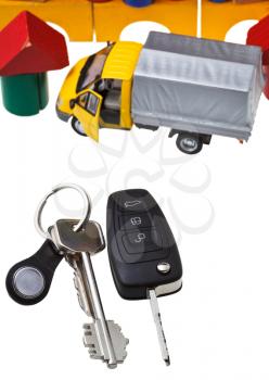 top view of door keys, vehicle key, new truck model and wooden block toy house isolated on white background