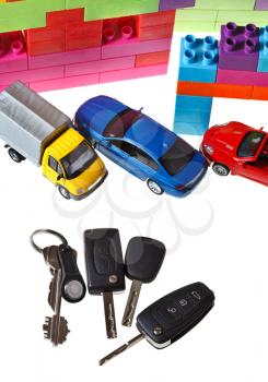 top view of door key, vehicle keys, three model cars and plastic block house isolated on white background