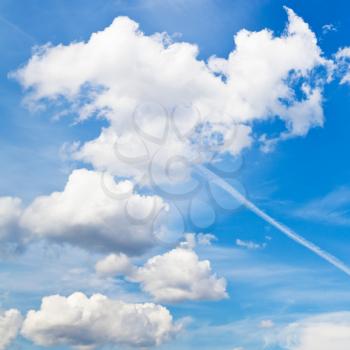 cloudscape with white fluffy clouds and trace of plane in blue sky in summer day
