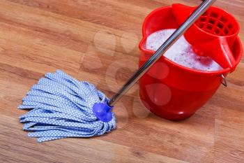 blue textile mop and red bucket on wooden floor