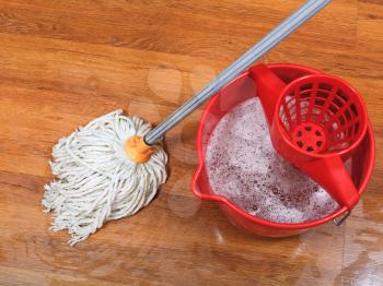 textile mop and red bucket on wooden wet floor