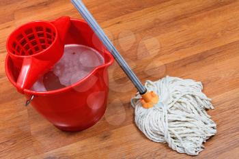 cleaning of floors by mop and red bucket with washing water