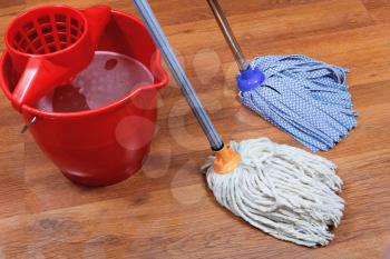 cleaning of wet floors by two mops and red bucket with washing water