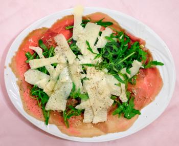 italian carpaccio with parmesan cheese and arugula on white plate