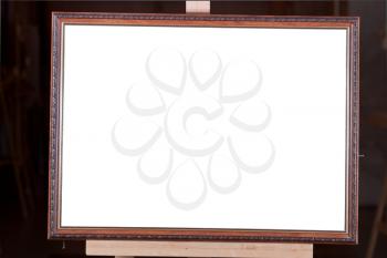 brown wooden picture frame with white cut out canvas on easel on black background