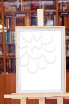 white canvas of simple picture frame on easel with clipping path and home library on background