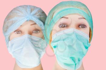 two women's dummy doctor heads wearing textile surgical cap and medical protective mask isolated on pinkbackground