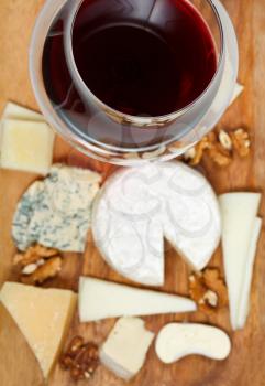 red wine glass and portion of sliced cheeses on wood plate