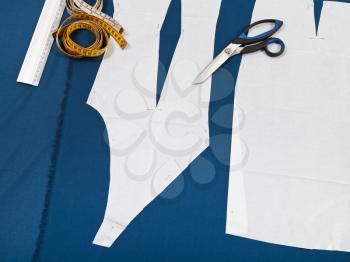 tailor tools and paper model of clothes on blue fabric for dress cutting