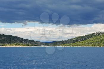 view of green lands of Dalmatia from Adriatic Sea under dark blue clouds, Croatia