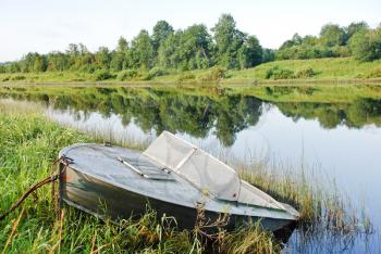 old boat on green shore of small river in summer day