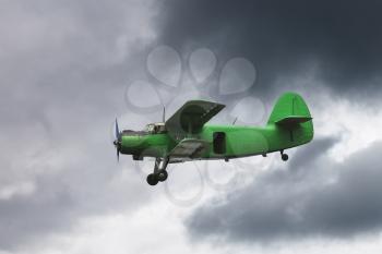 small green airplane flying in dark grey sky in summer day