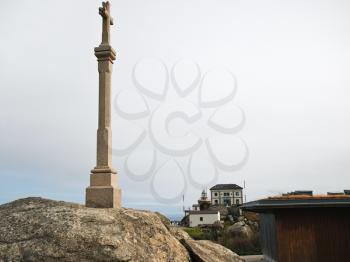 Christian cross and view of lighthouse on Cape Finisterre - the end of Way of St. James, Galicia, Spain