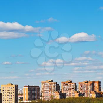 white clouds in blue sky over brick apartment houses in spring