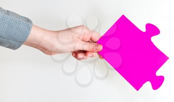pink puzzle piece in female hand on grey background