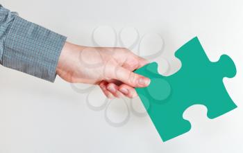 female hand holding green puzzle piece on grey background