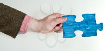 blue painted puzzle piece in male hand on grey background