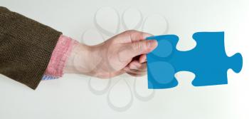 male hand holding blue puzzle piece on grey background