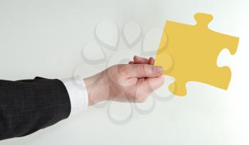 male hand holding yellow puzzle piece on grey background
