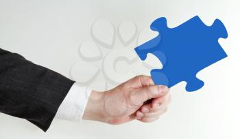 male hand holding blue puzzle piece on grey background