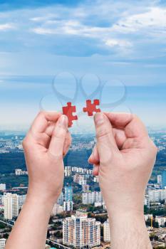 male and female hands with little puzzle pieces with modern urban residential district background