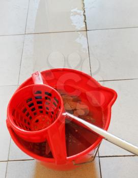 swab in red bucket with washing water and cleaning tile floor