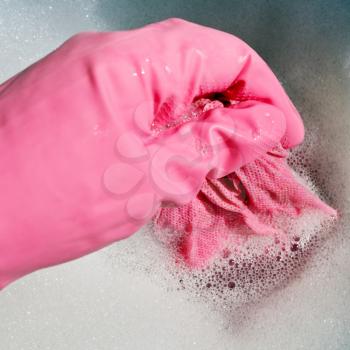 hand in pink rubber glove wrings out wet cloth from foamy water