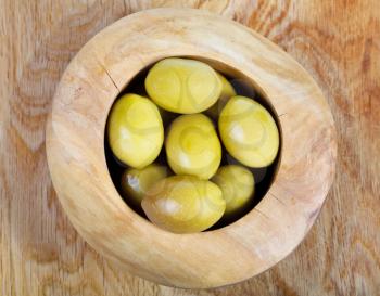 above view of green olives in wooden bowl on wood plate