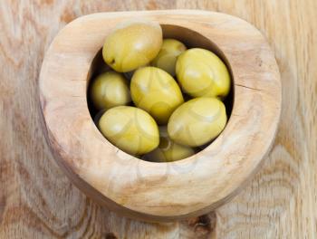 top view of green olives in wooden bowl on wood plate