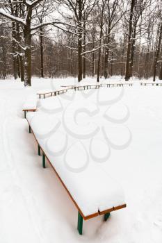 snow on benches in city park in winter