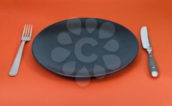 empty black plate with fork and knife set on red background