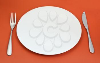 empty white porcelain plate with fork and knife set on red background