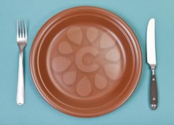 top view of empty ceramic brown plate with fork and knife set on green background