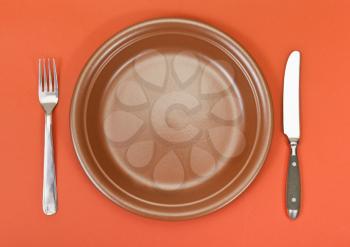 top view of empty ceramic brown plate with fork and knife set on red background