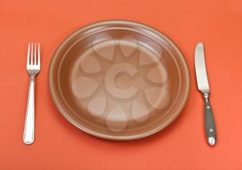 above view of empty ceramic brown plate with fork and knife set on red background