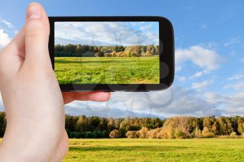 travel concept - tourist taking photo of green meadow in sunny autumn day of on mobile gadget