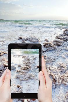 travel concept - tourist snapping photo of crystal salt on Dead Sea beach on mobile gadget, Jordan