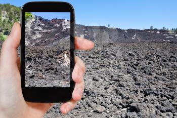 travel concept - tourist taking photo of hardened lava flow on slope of Etna, Sicily on mobile gadget, Italy