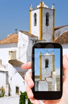 travel concept - tourist taking photo of white old Santiago church in Tavira town, Portugal on mobile gadget