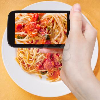 photographing food concept - tourist taking photo of spaghetti with spicy tomato sauce on white plate on mobile gadget, Italy