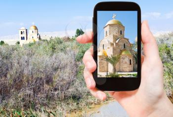 travel concept - tourist taking photo of church in Jordan river valley on mobile gadget