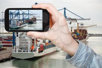 travel concept - tourist taking photo of Copenhagen cargo seaport on mobile gadget at sunrise