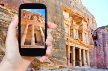 travel concept - tourist taking photo of Treasury Monument temple in rock in ancient city Petra on mobile gadget, Jordan