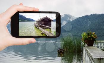 travel concept - tourist taking photo of shed on Schliersee lake in Bavarian Alps on mobile gadget, Germany