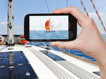 travel concept - tourist taking photo of yacht with red sail in blue Adriatic sea, Dalmatia, Croatia on mobile gadget