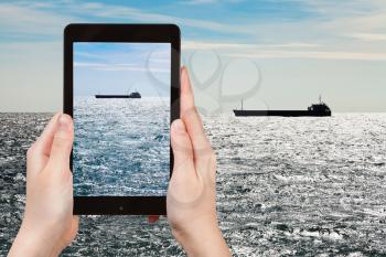 travel concept - tourist taking photo of ship in Black sea in autumn evening on mobile gadget
