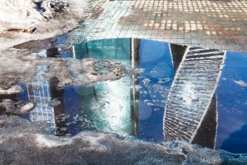 spring urban landscape with melting snow puddle and house reflection in Moscow City