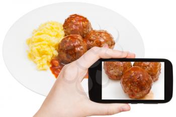 photographing food concept - tourist takes picture of roasted meatballs under meat sauce and mashed potato on plate on smartphone, Sweden